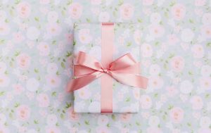 Gift with a floral wrap and a pink ribbon surrounded by floral gift wrapping paper.