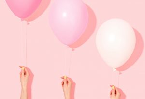 Two pink and one white balloons being held by female hands with yellow fingernails.