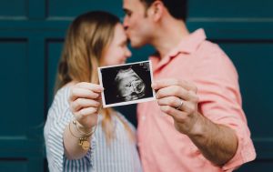 A man kissing a woman’s forehead, they’re both holding an ultrasound.