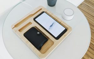 A bamboo phone and wallet holder on top of a white table. To its side is a tiny plant.