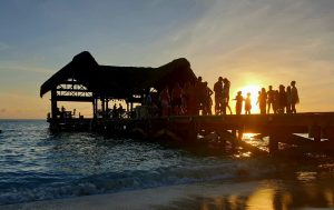 Sun setting on a pier cabana party full of people.