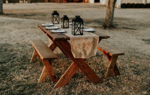  A wooden table with candles and plates has a barn and string lights on the background. 