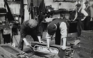 Two men working in a factory with two men behind looking at them