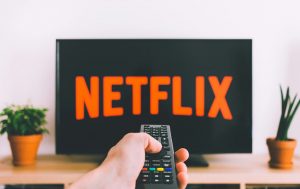 TV with Netflix cover with plants to its sides and a male hand holding a remote control.