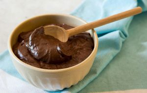 Tiny bowl with chocolate mousse and a wooden spoon on top of a blue towel.