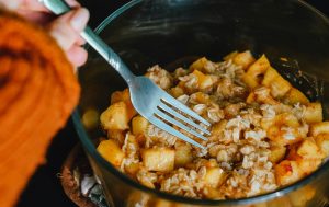 A woman holding a fork preparing a peach crisp in a bowl.