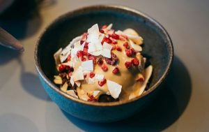 A black bowl full of ice cream with berries and coconut flakes.