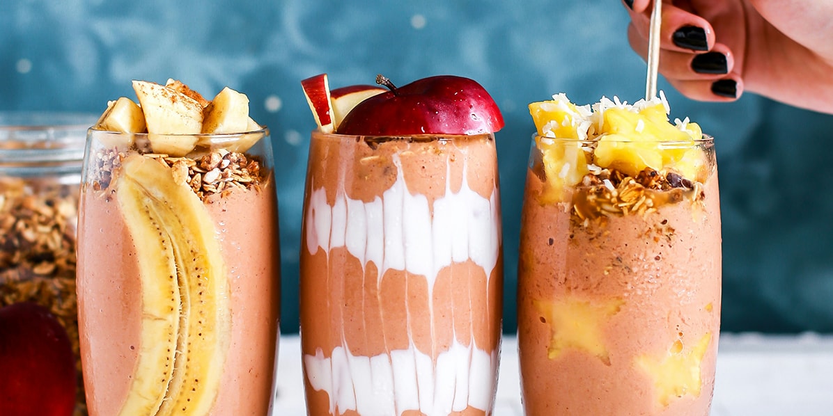 Three glasses full of mousse-like products with fruits and a female hand holding a spoon to one of them.