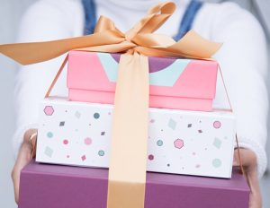 A woman holding a stack of three Woops! French macaron boxes tied together by a golden ribbon.