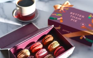 A box full of nine assorted has a macaron box with a Thanksgiving sleeve and a cup of coffee to the side.