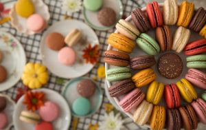 A plate full of assorted macarons has other plates full of macarons, tiny pumpkins, and flowers to the side.