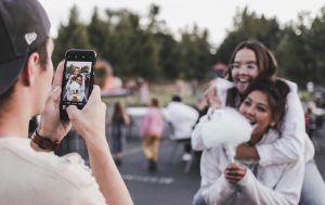 A man taking a photo of two smiling women holding cotton candy.