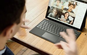 Person video chatting with four people on a tablet at a wooden table.