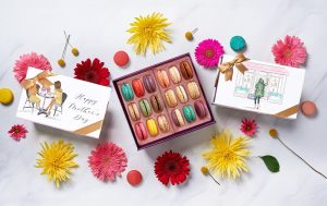 3 macaron boxes surrounded by colorful flowers.