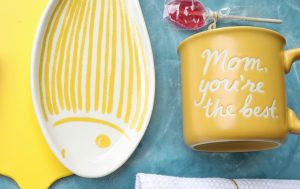 A yellow fish-shaped dish and a yellow mug sit on a blue surface.