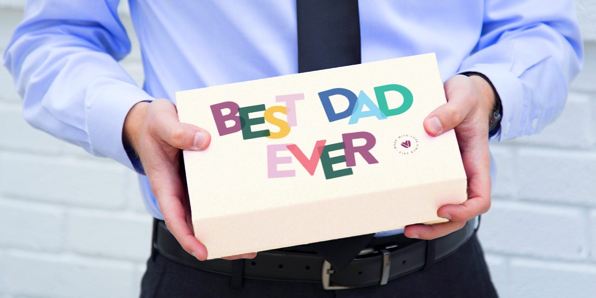 Man in a shirt holding a box of macarons with a "Best Dad Ever" sleeve on it.