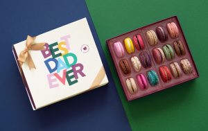 Two boxes of macarons, one opened with different macaron colors, the other on is close and has the “Best Dad Ever” edition.
