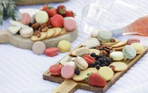 A picnic setup with glasses, rosé and cheese boards with fruits, nuts, and macarons.