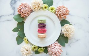 A white plate features 4 assorted macarons, surrounded by leaves and flowers.