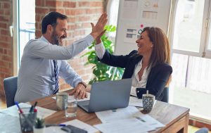 Two middle-aged business workers smiling and giving a high five at an office.