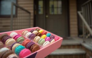 Someone delivering an open Woops! macaron box to a front door. 