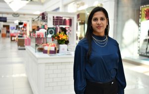 Woman in a blue blouse standing in front of a Woops! Kiosk inside a mall.