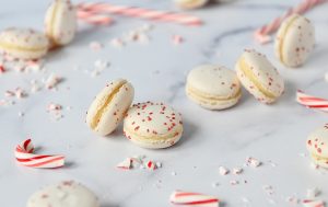 Candy Cane macarons sprinkled with crushed candy cane pieces scattered on a marble surface with candy canes around them.
