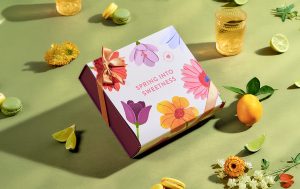 A box of macarons with a “Spring into sweetness” sleeve with some limes and flowers around. 