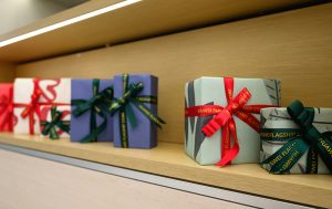 Colorful gift boxes wrapped with red and green ribbons displayed on a wooden shelf under warm lighting.
