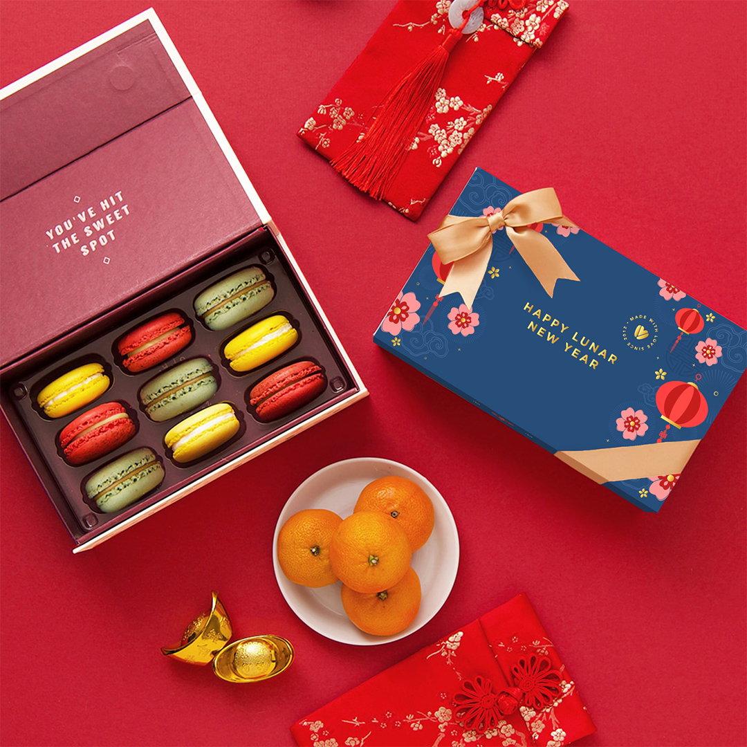 Build Your Own Year Of The Horse Box - 1080x1080 Lunar New Year macaron gift set with an open box of colorful macarons, mandarins, gold ingots, and festive red envelopes on a red background.