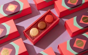 Assorted Woops! macaron gift boxes arranged on a pastel background, with one open box displaying three colorful macarons.