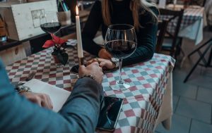 Couple holding hands at a candlelit restaurant table with glasses of red wine.